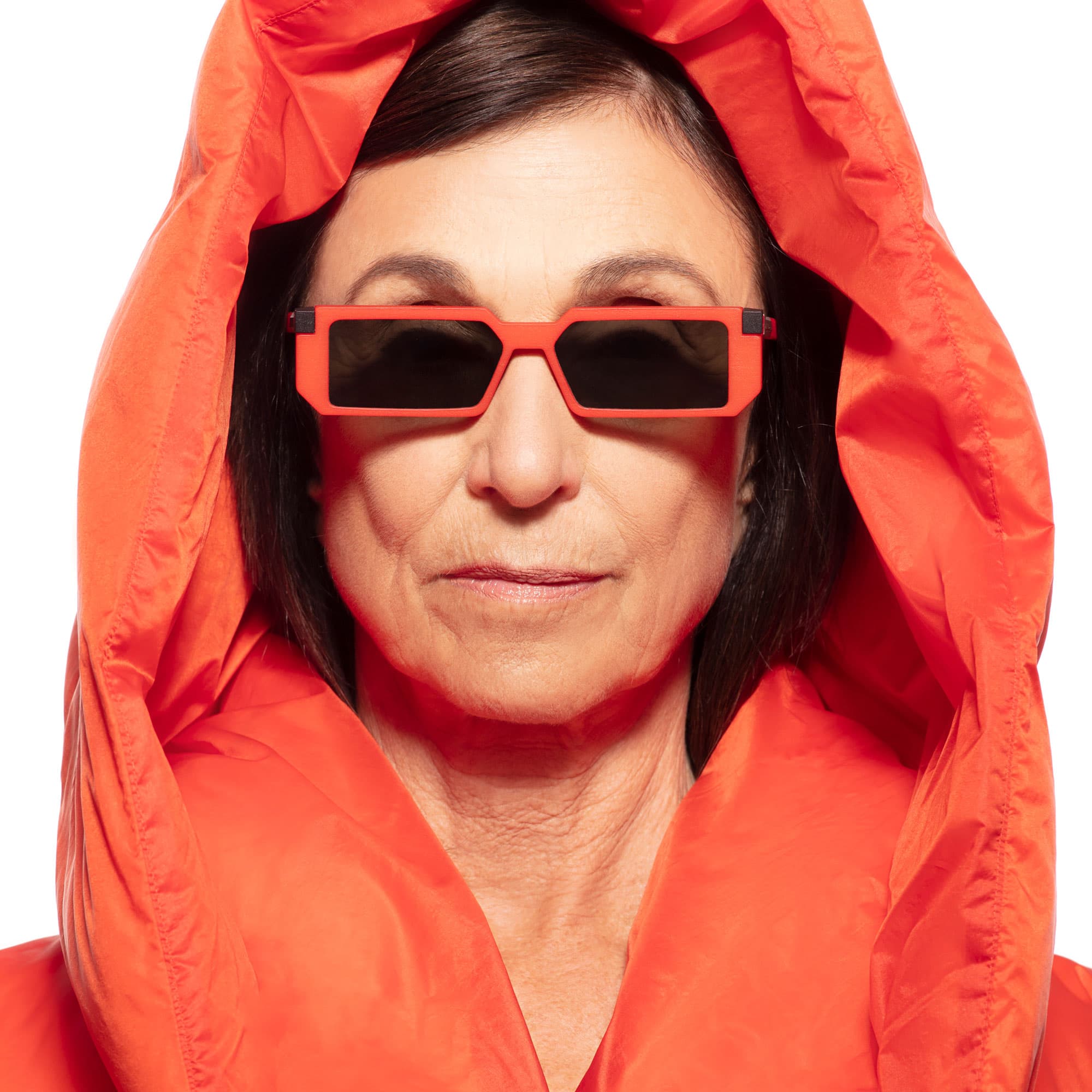 A woman in an orange hood wearing rectangular orange VAVA sunglasses, close-up portrait